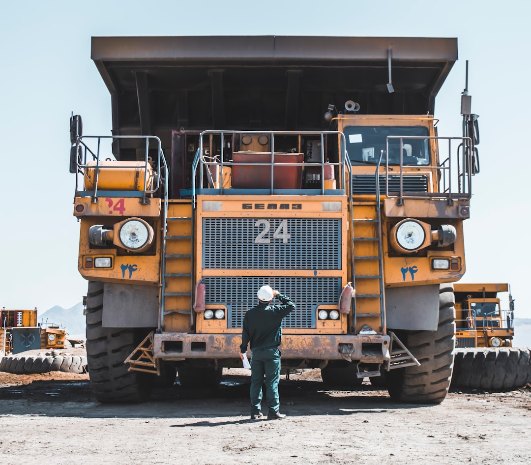 man-in-brown-jacket-standing-beside-yellow-truck-lhi9na4u7hg